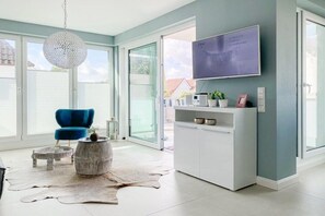 A modern living room with a blue chair, a round table, a mounted TV, and a white cabinet. - Holiday apartment with 2 bedrooms (Timmendorfer Strand)