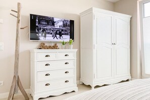 A bedroom with a bed, a white dresser with drawers, a television mounted on the wall, and a white wardrobe. - Holiday apartment with 2 bedrooms (Timmendorfer Strand)