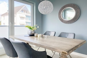 Ein Essbereich mit Holztisch, vier Stühlen, einer Blumenvase, einem strukturierten, kugelförmigen Lichtarmaturen und einem runden Spiegel an der Wand.