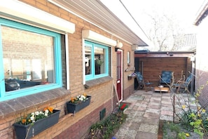 A brick house with a small backyard patio, a wooden deck, and a red door. - Holiday cottage with 2 bedrooms (Petten)