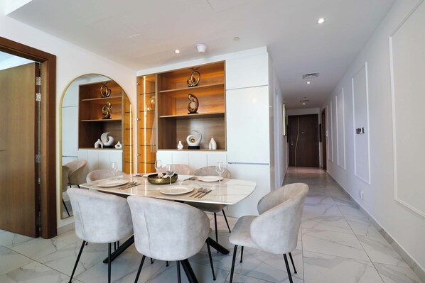 A dining area with a marble table, four chairs, and a modern kitchen with wooden shelves. - Rentico | 1BR Burj Khalifa & Canal View Balcony (Dubai)