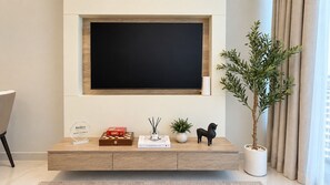A modern living room with a mounted TV, a wooden console table, a potted plant, and a small statue. - Rentico | Skyhills Studio | Pool, Sauna, Gym, BBQ (Dubai)