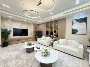 A modern living room with a flat-screen TV, two white sofas, and a marble coffee table with floral arrangements. - Rentico | Skyhills Studio | Pool, Sauna, Gym, BBQ (Dubai)