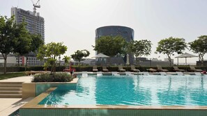 Una piscina con sillones de descanso y un edificio moderno al fondo.