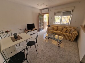 A living room with a sofa, a television, a dining table with chairs, and a glass coffee table. - ☀️ El Rincon S&E – Your little corner of paradise between golf, the beach, and the sun (San Miguel de Salinas)