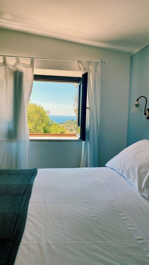 Ein Schlafzimmer mit einem Bett, einem Fenster mit Vorhängen und Blick auf Grünflächen.