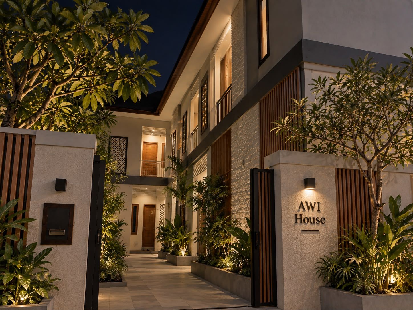 Un hotel moderno con una entrada bien iluminada, una placa con el nombre visible y un camino vallado que lleva al edificio.