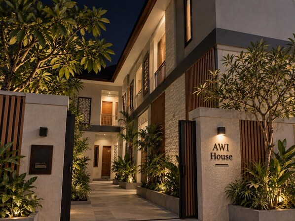 A modern hotel with a well-lit entrance, a visible nameplate, and a gated pathway leading to the building. - Awi House (Jimbaran)