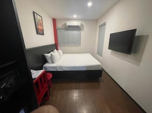 A bedroom with a bed, a TV mounted on the wall, a window, and a red chair. - Silver Quarter Hanoi Hotel (Hanoi)