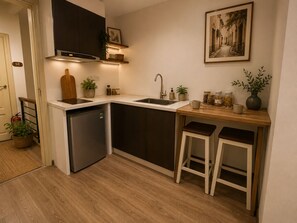 A compact kitchen with a dishwasher, a sink, and a small countertop. There are two stools and a potted plant. - Quarter Balcony Apt 3Brs . Free Laundry . Sleeps 8 by Anamoi (Hà Nội)