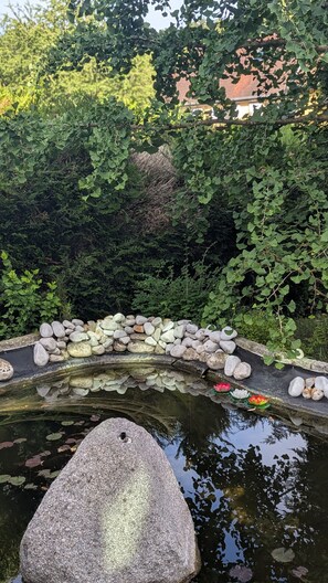 A pond with a large rock in the foreground, surrounded by a stone wall and lush greenery.