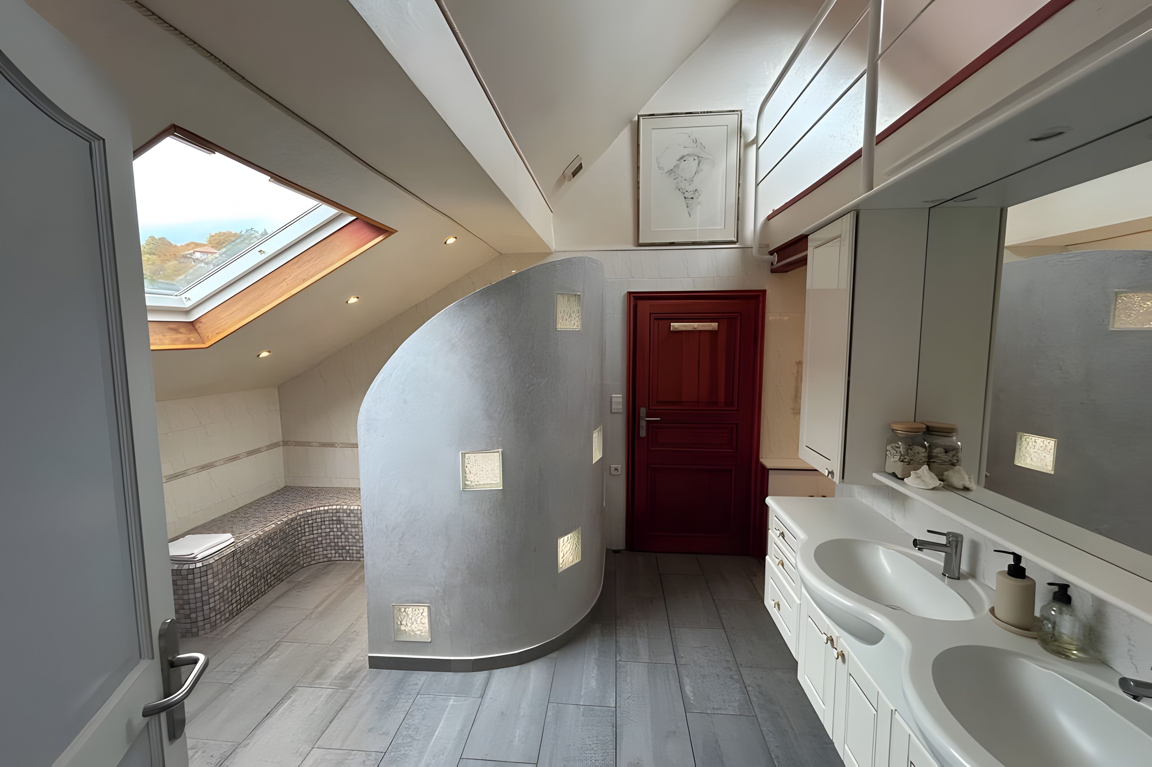 Un baño moderno con tragaluz, un espejo grande y una puerta roja.