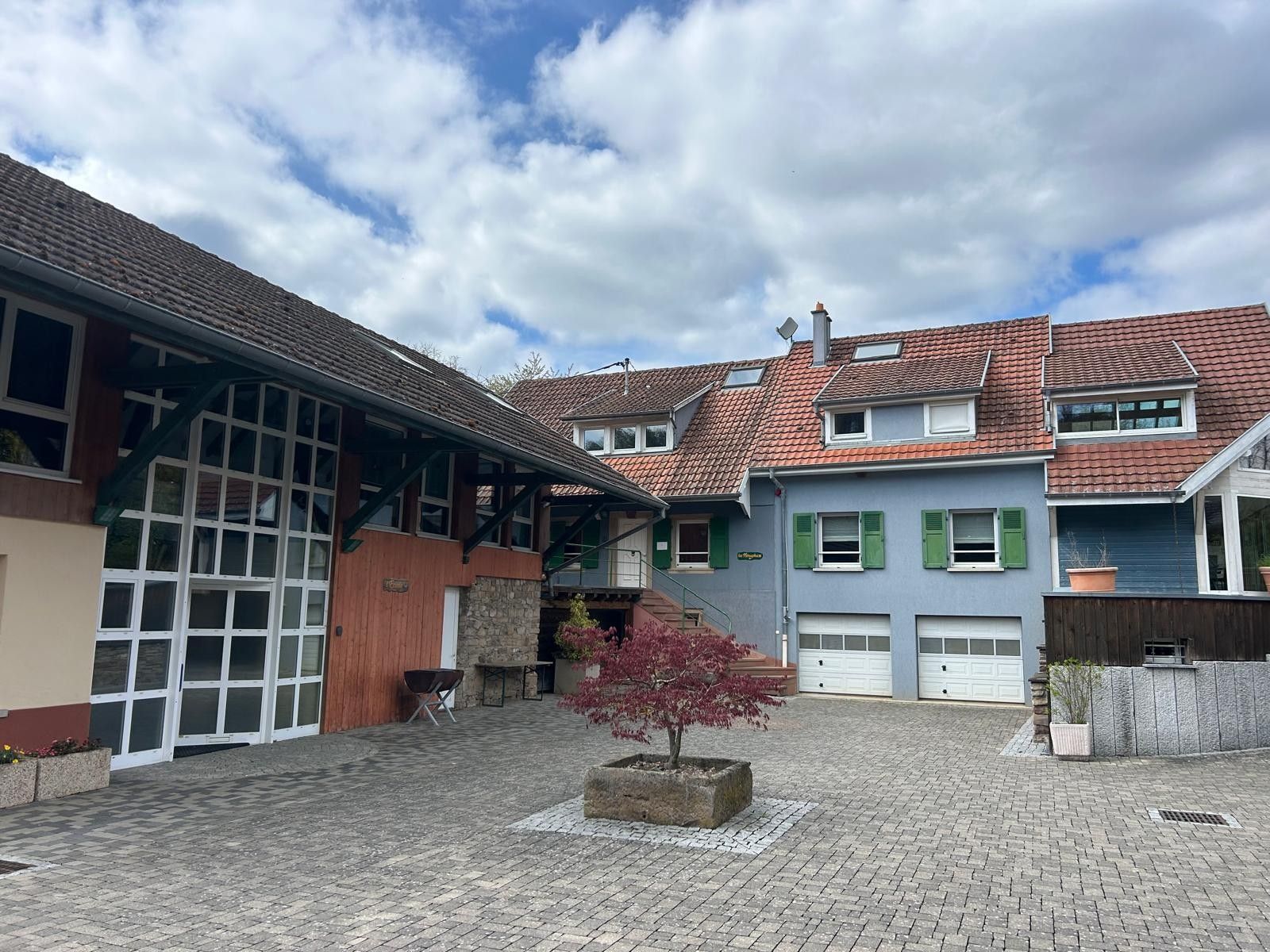 Ein Innenhof mit einem Baum mit roten Blättern, einer Steinsitzbank und einem Gebäude mit einer Garagentür.