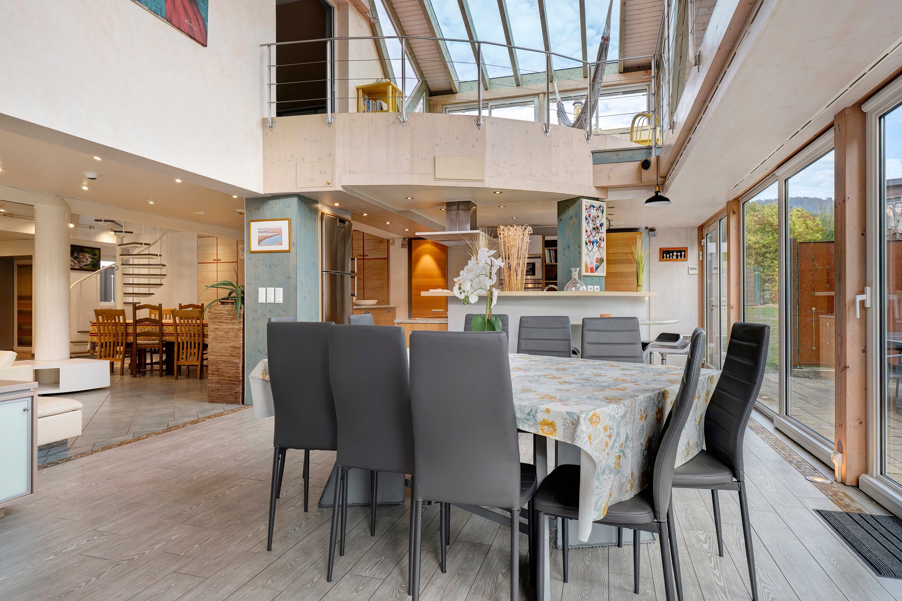 Un comedor amplio con techo alto y luz natural, una cocina con electrodomésticos modernos y vistas al exterior.