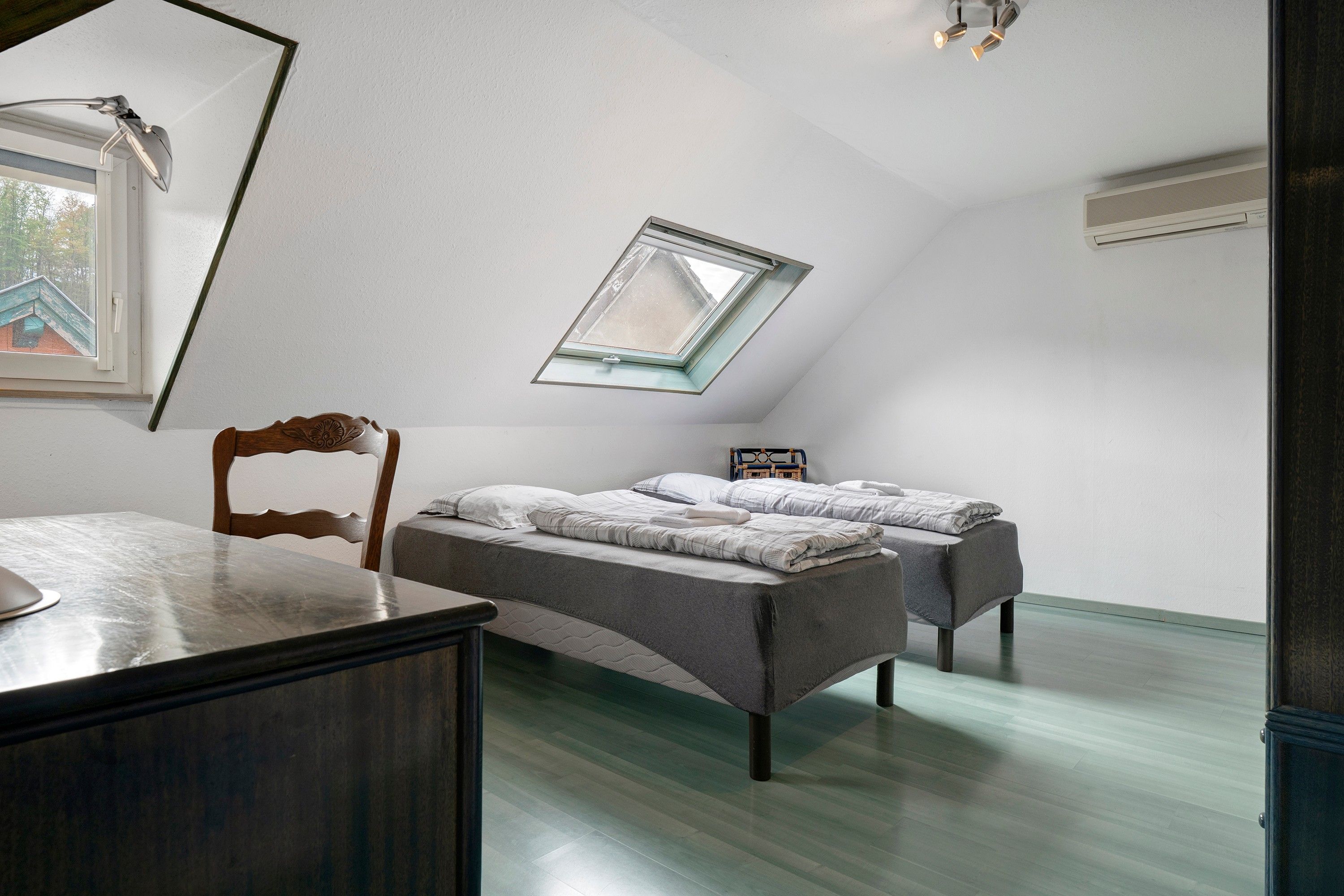 A bedroom with a sloped ceiling, a skylight, a bed, a chair, and a desk.