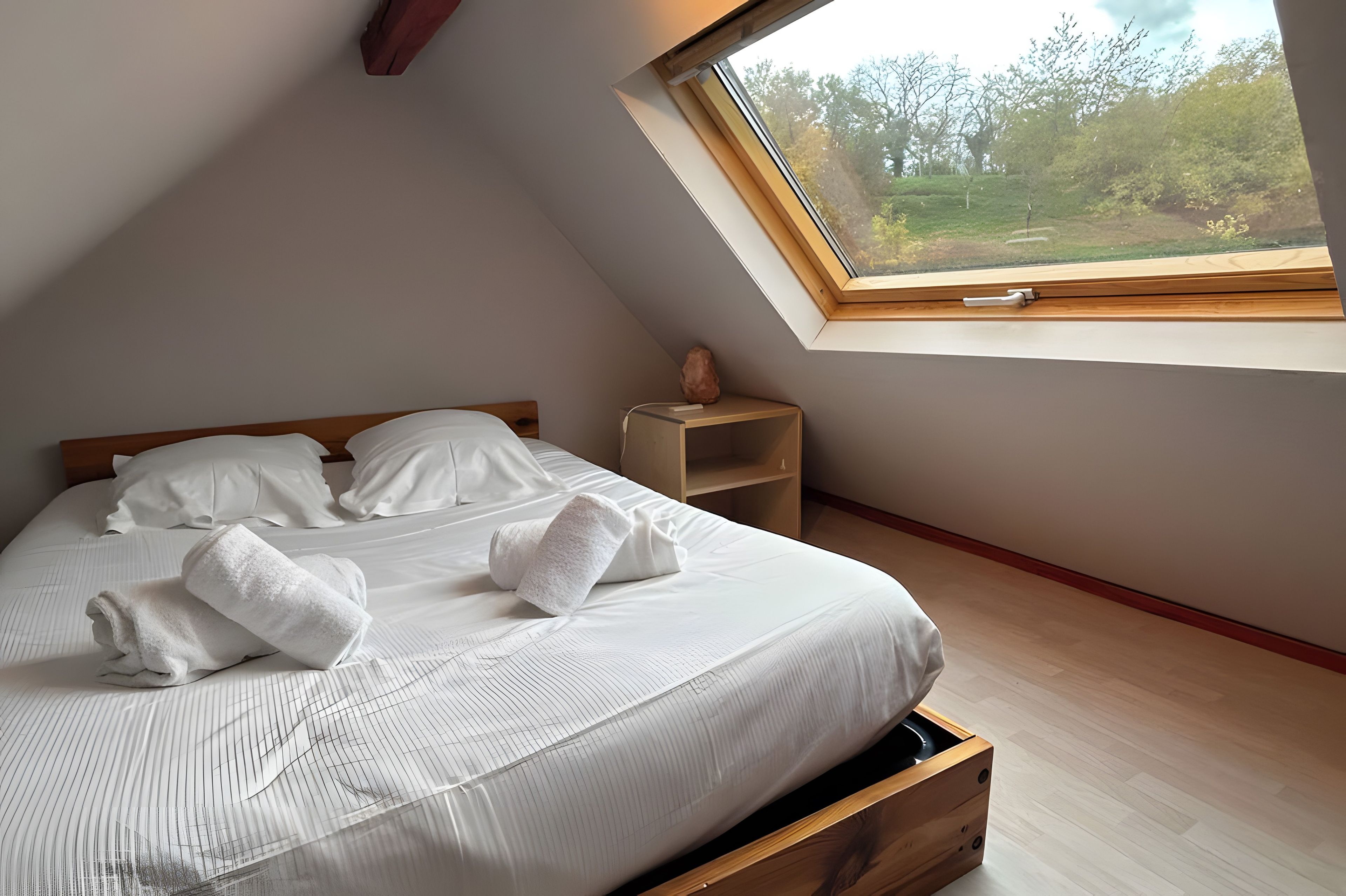 Un dormitorio con cama, mesita de noche, ventana y vistas al exterior.