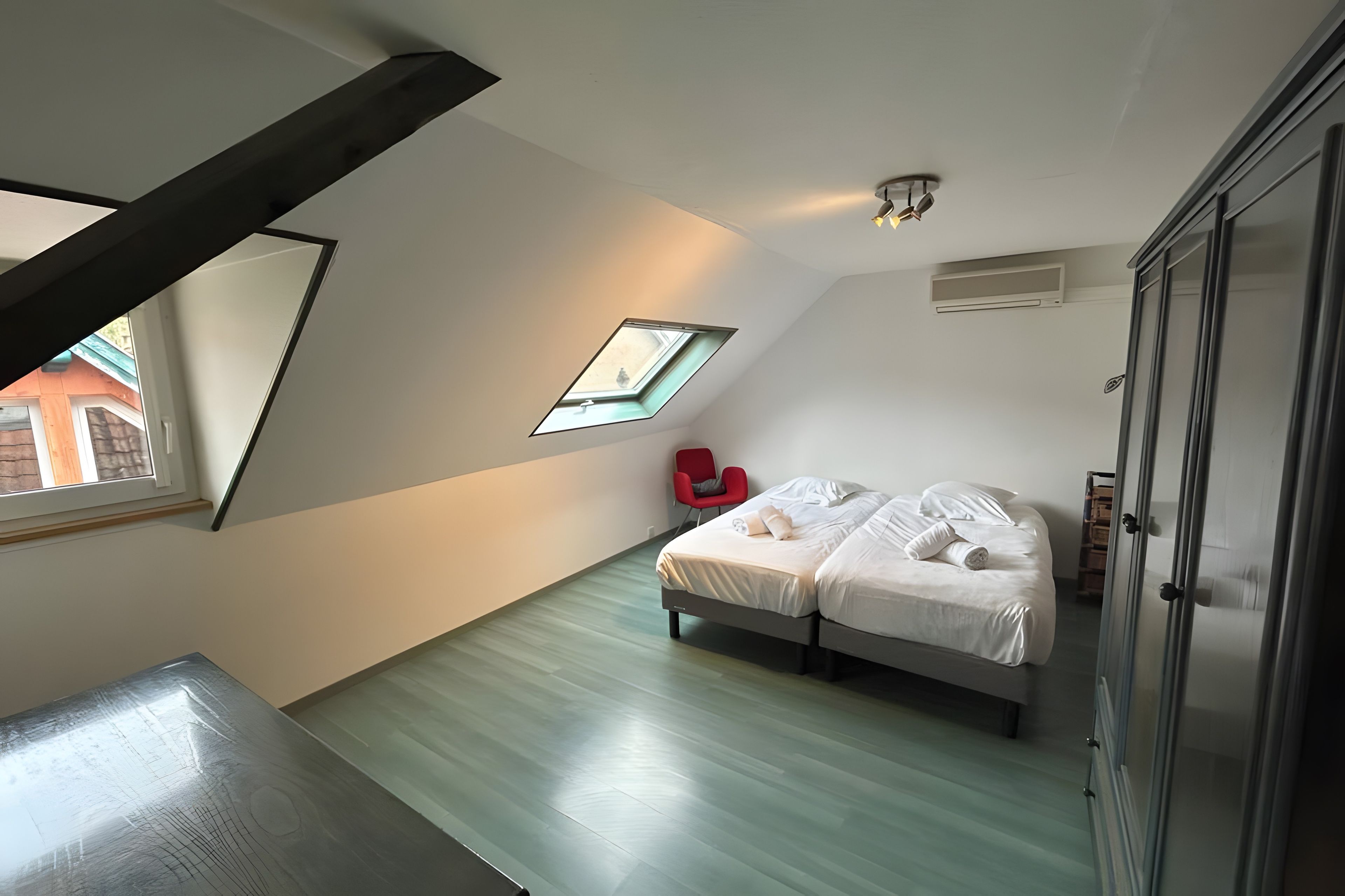 Een slaapkamer met dakraam, een bed, een rode stoel en een kledingkast.
