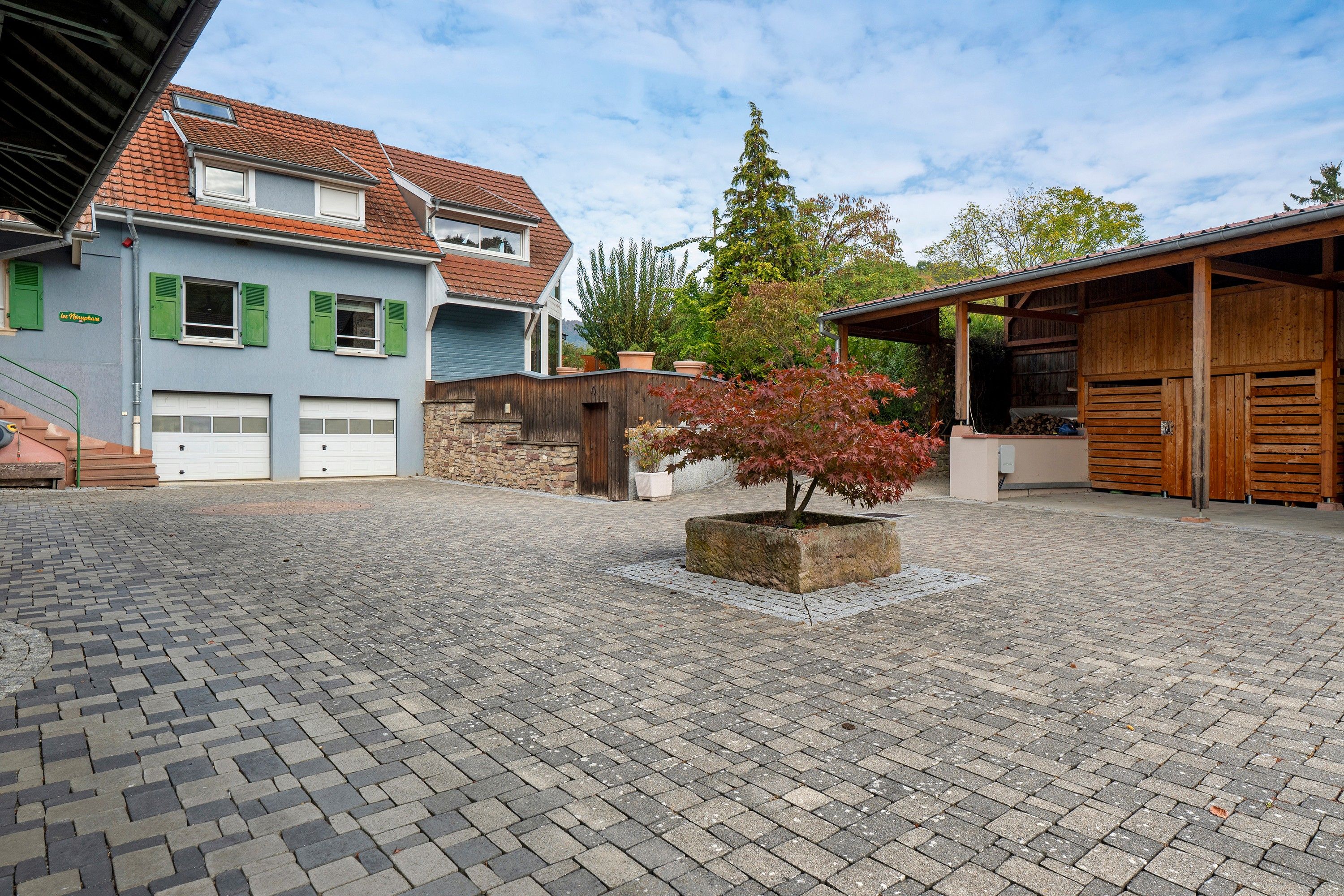 A courtyard with cobblestone paving, a wooden structure, and a building with green shutters.