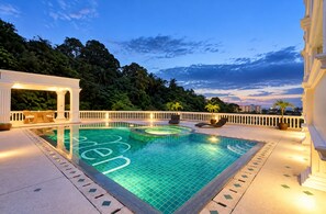 Piscina com vista para uma área arborizada e edifícios ao fundo.