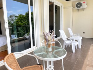 Ein Balkon mit einem Glastisch, Korbstühlen und einem weißen Kunststoffstuhl.