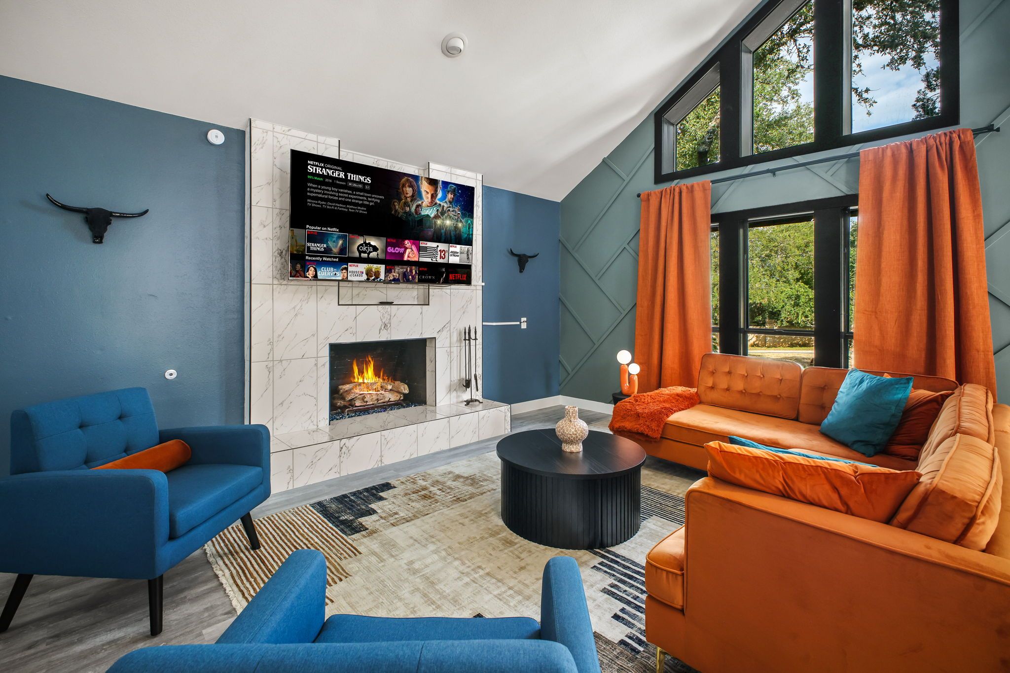 A modern living room with a fireplace, blue and orange furniture, and a large window.