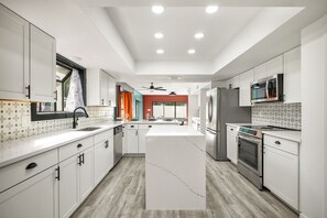 A modern kitchen with white cabinetry, a central island, and a built-in oven. - Pool Haven | Hot Tub Game Room Fire Pit Mini Golf (San Antonio)