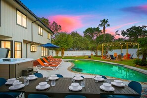 Ein Garten mit Swimmingpool, Essbereich im Freien und überdachter Sitzgelegenheit.