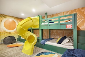 A bunk bed with a yellow slide, a patterned wall, and a maximum weight limit sign. - Pool Haven | Hot Tub Game Room Fire Pit Mini Golf (San Antonio)