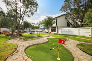 A miniature golf course with a house in the background. - Pool Haven | Hot Tub Game Room Fire Pit Mini Golf (San Antonio)