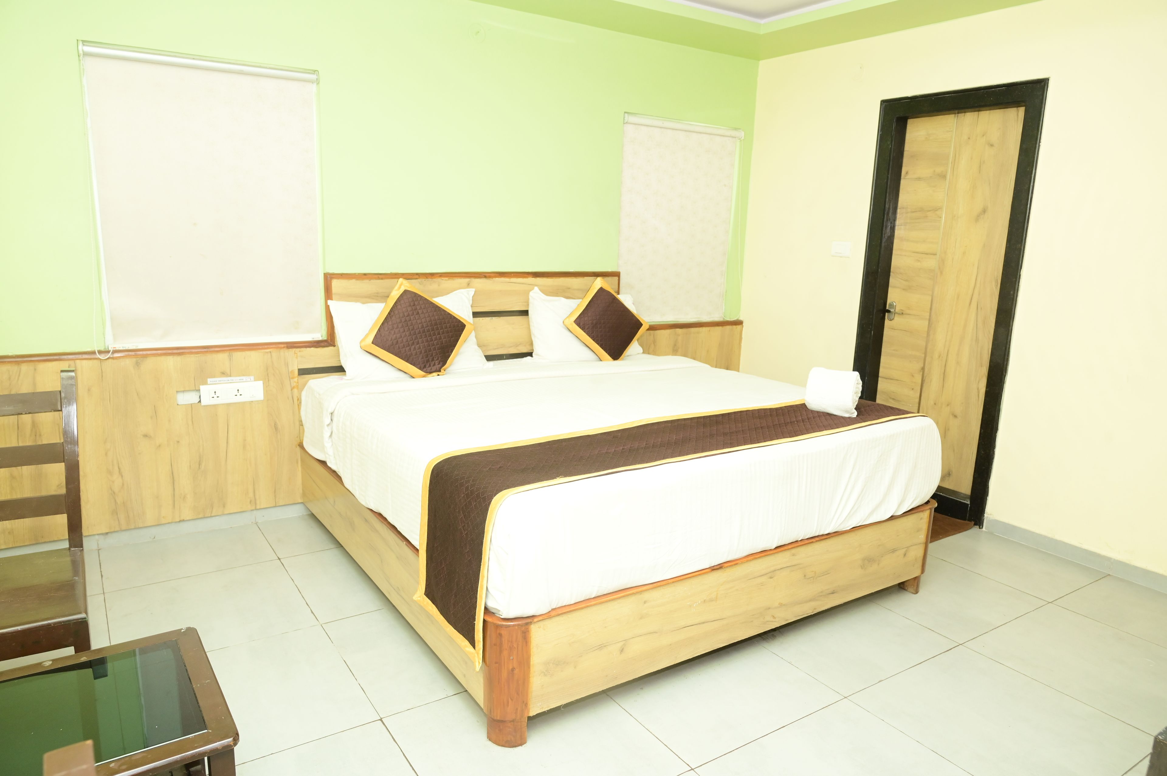 A neatly made bed with a wooden frame and white bedding, a wooden chair, and a small table with a glass top.
