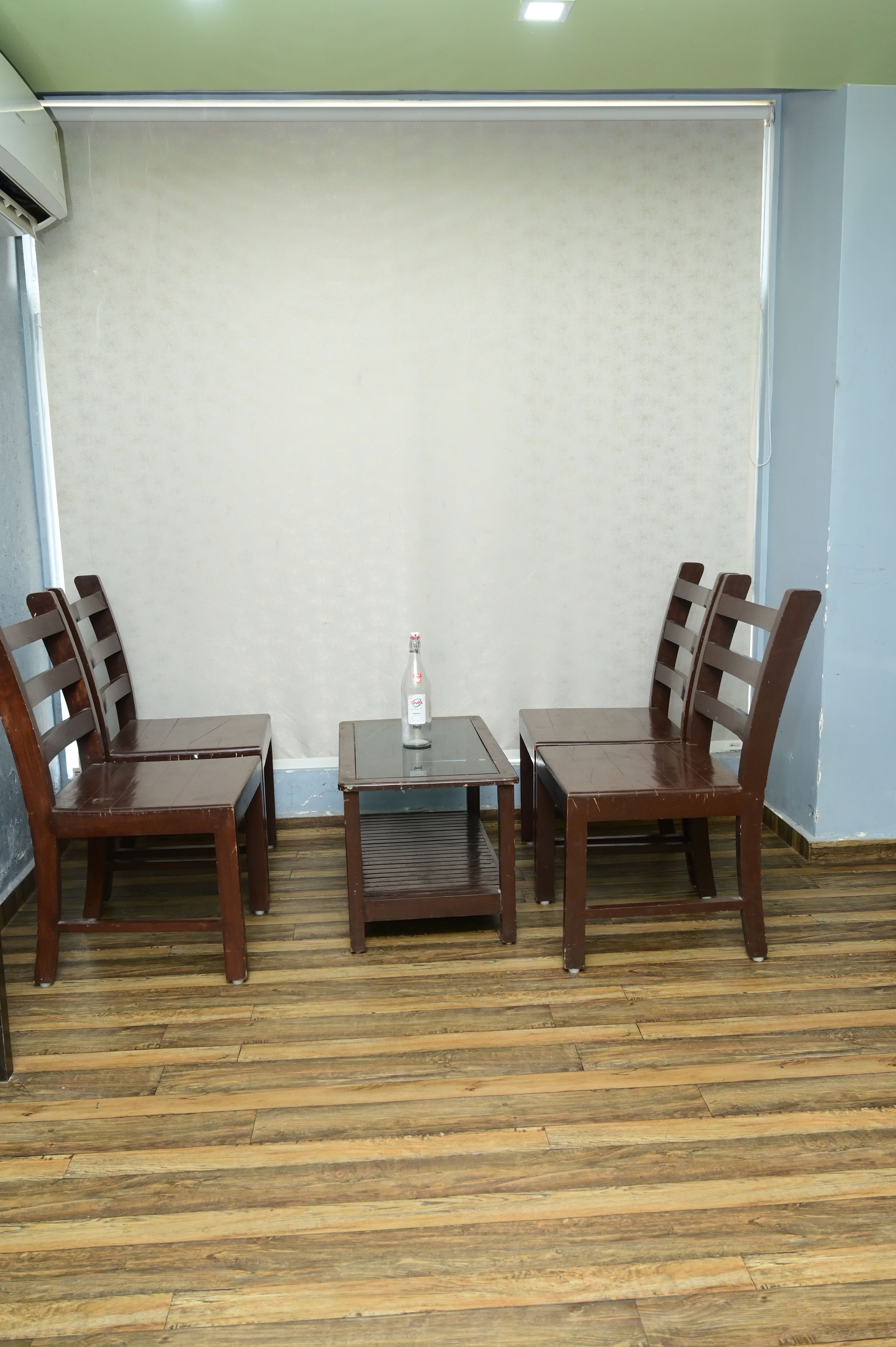 Una habitación con piso de madera, una mesa con cuatro sillas y una botella sobre la mesa.