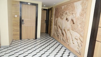 Een gang met een patroon in de vloer, houten deuren met nummering en een gedetailleerde wanddecoratie.