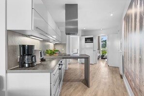 A modern kitchen with a central island, built-in appliances, and a view into the adjacent living area. - Spacious holiday apartment with luxury features and covered terrace near the Bal (Lübeck)