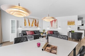 Moderni olohuone, jossa on ruokapöytä, sohvia ja taideteoksia seinillä.
