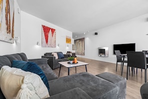 Ein modernes Wohnzimmer mit einem grauen Sofa, einem Esstisch und einem Flachbildfernseher.