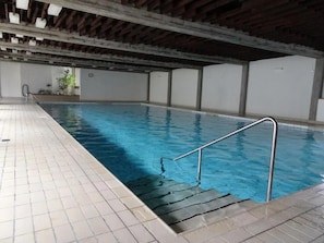 An indoor swimming pool with a tiled floor and a metal handrail. - Cozy vacation rental for families with mountain views, midday sun, a pool, and a sauna (Davos)