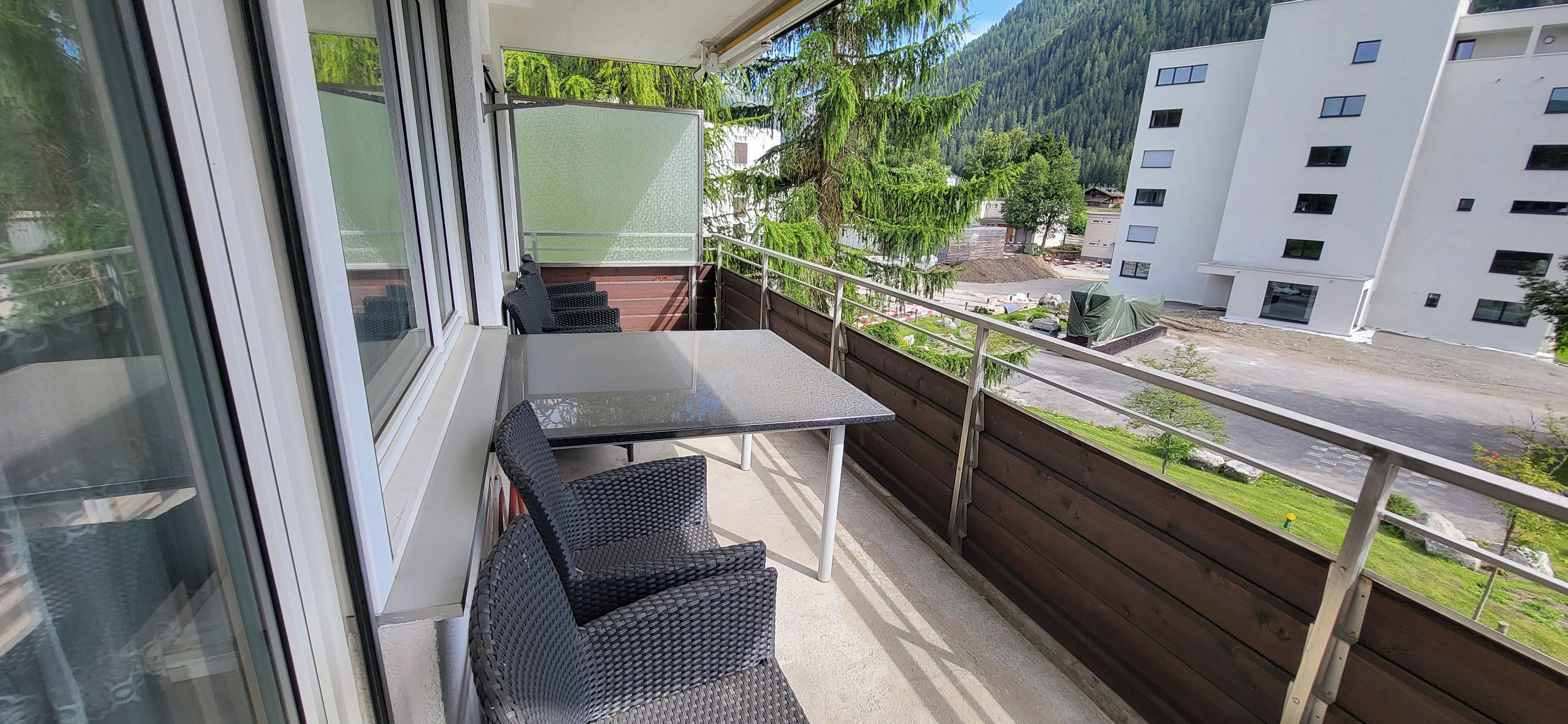 A balcony with a table and chairs, overlooking a street and buildings.