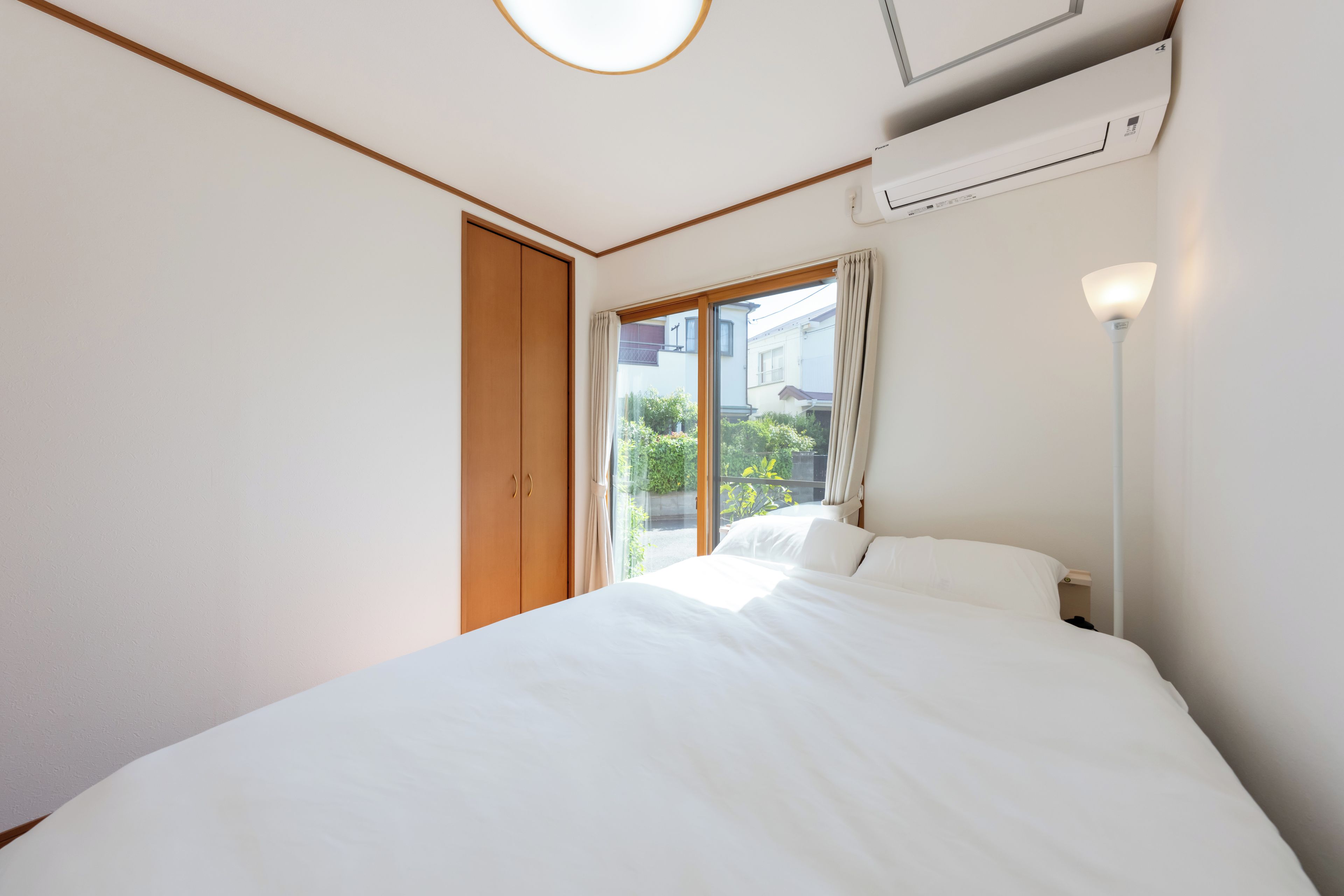 A hotel room with a bed, a window with curtains, an air conditioning unit, and a bedside lamp.