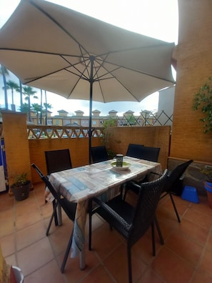 An outdoor patio with a table and chairs, an umbrella, and a view of buildings in the background. - 3-bedroom townhouse with a pool and a paddle tennis court (lepe)