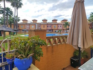 A balcony with potted plants, a pool, and a building with a tiled roof in the background. - 3-bedroom townhouse with a pool and a paddle tennis court (lepe)