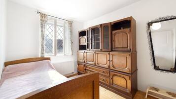 Une chambre avec un lit en bois, une grande armoire en bois, une fenêtre avec des rideaux et un miroir au mur.