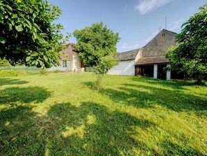 A grassy yard with a small tree, a white building with a sloped roof, and a wooden fence.