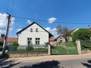 Een wit huis met twee verdiepingen, met een groene omheining en een stenen muur.