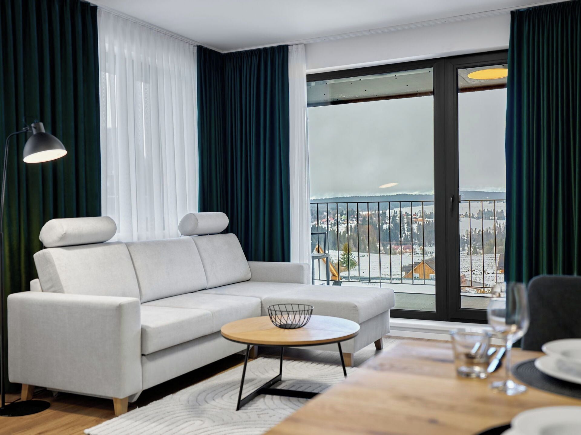 Ein modernes Wohnzimmer mit einer Couch, einem runden Couchtisch und Blick auf eine verschneite Landschaft durch große Fenster.
