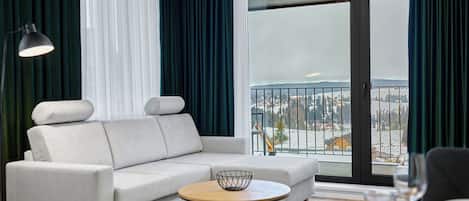Een moderne woonkamer met een bank, een ronde salontafel en een uitzicht op een besneeerd landschap door grote ramen.