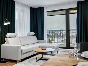 Ein modernes Wohnzimmer mit einer Couch, einem runden Couchtisch und Blick auf eine verschneite Landschaft durch große Fenster.