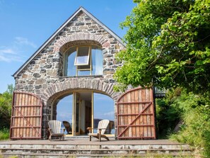 Ein Steinhaus mit einem großen Rundbogenportal, zwei Holztoren und einer Terrasse mit Sitzgelegenheiten.