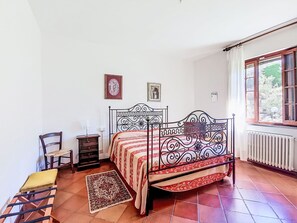 Ein Schlafzimmer mit einem Himmelbett, einem Sessel, einem kleinen Tisch und einem Fenster mit Vorhängen.