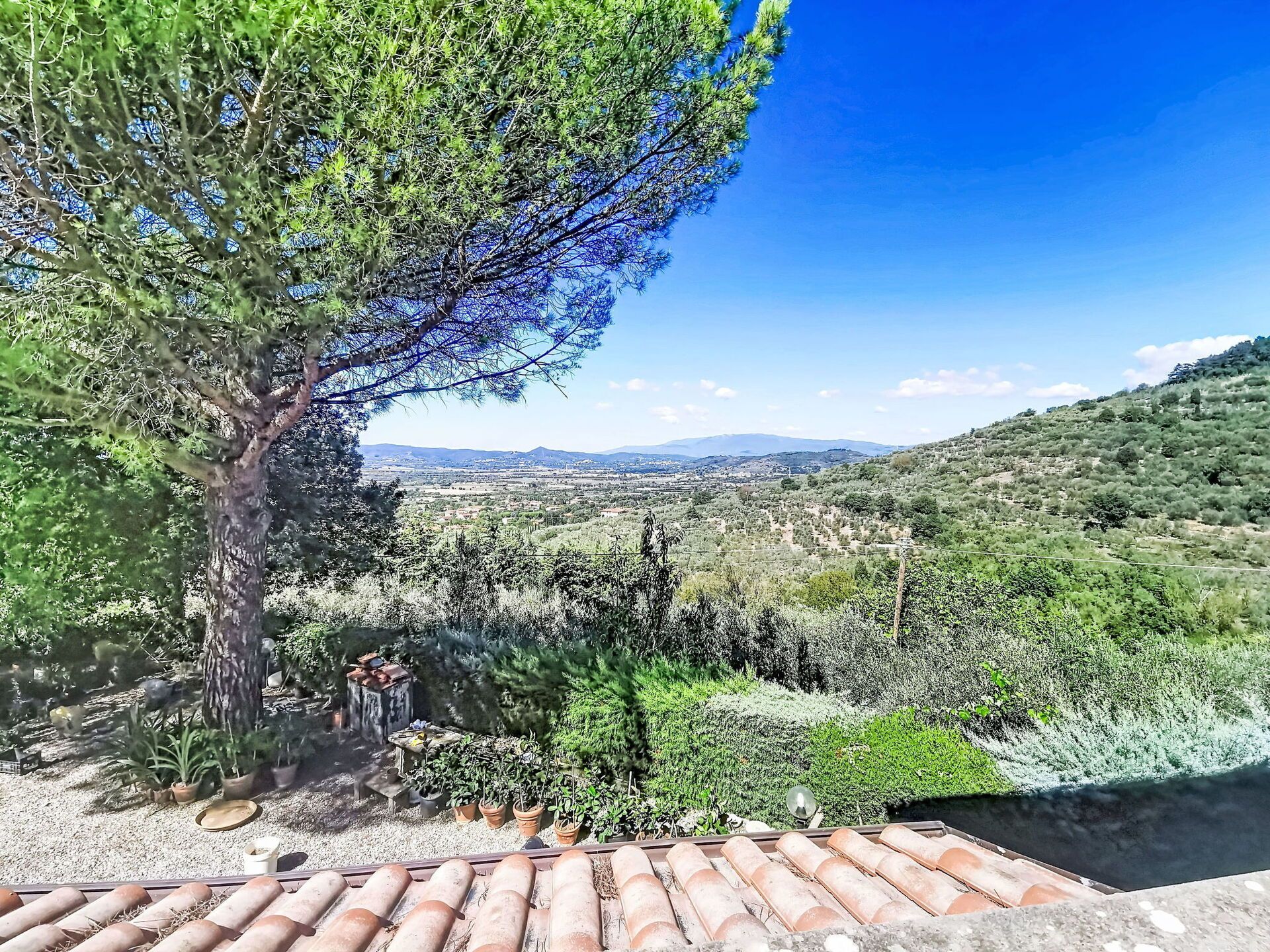 Vista desde una terraza con tejado de baldosas, que da a un valle con vegetación y montañas al fondo.
