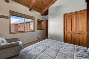 A bedroom with a large bed, a window, a wooden door, and a chair. - Ski in/Ski out- Timber Ridge 28 (Mammoth Lakes)